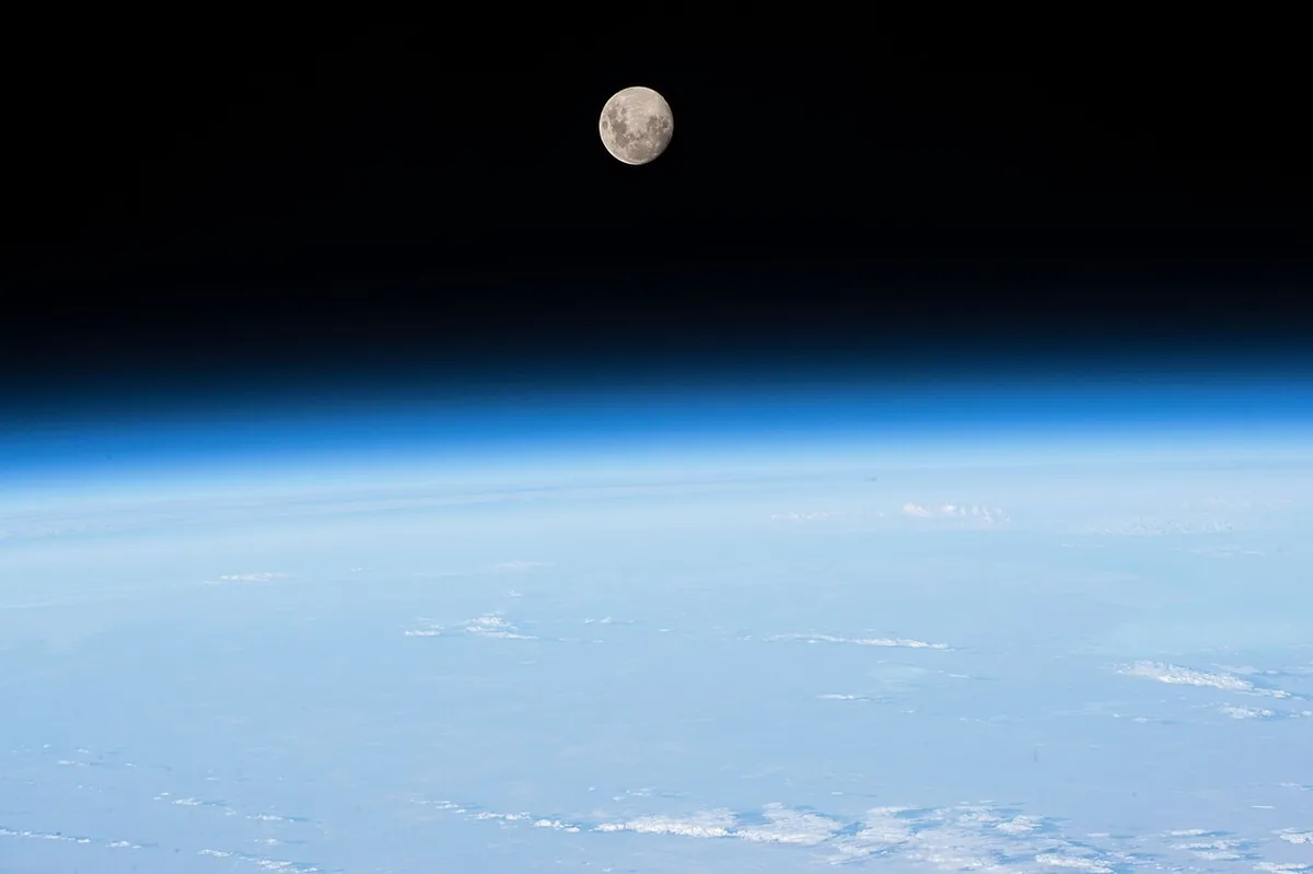 Fine couche bleue de l'atmosphère terrestre vue de profil depuis la Station spatiale internationale, avec la Lune au-dessus