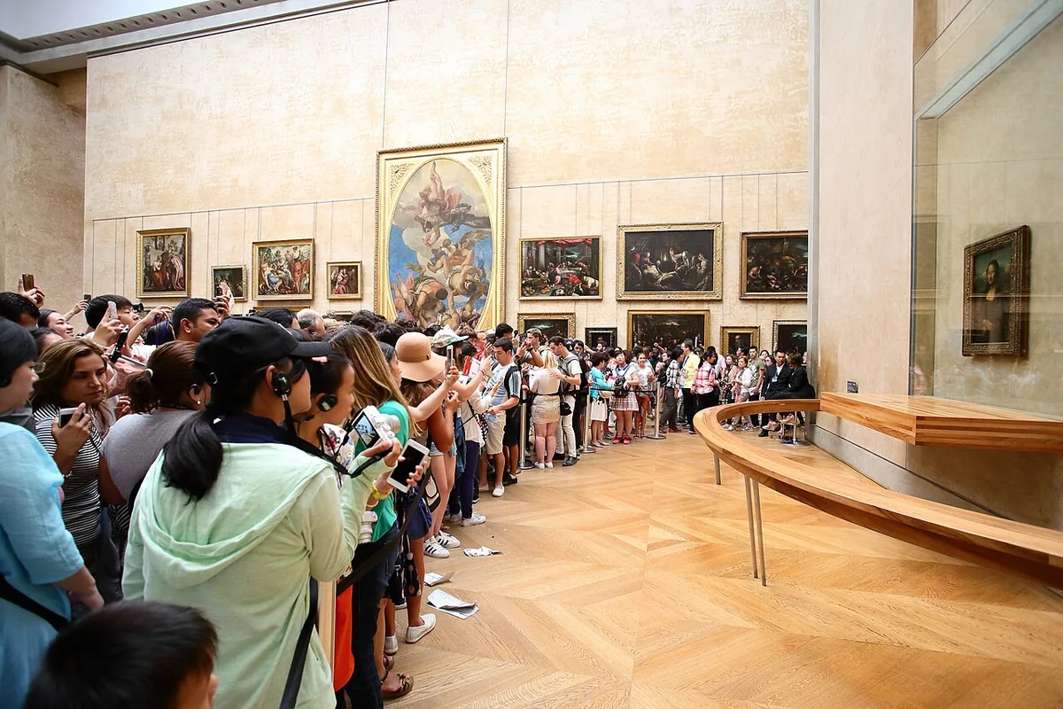 Foule dense de visiteurs smartphones levés dans la salle des États du Louvre devant la Joconde protégée