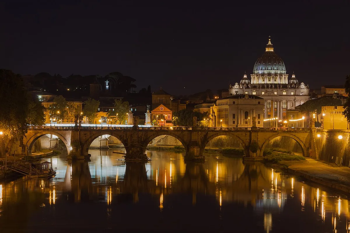 Le pont Saint-Ange illuminé sur le Tibre la nuit, avec le dôme de la basilique Saint-Pierre en arrière-plan